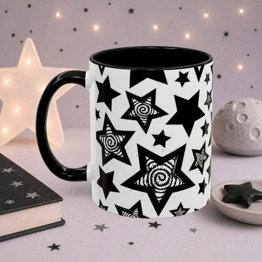 Monochrome star mug with repeating black celestial stars and spiral artwork, black accent handle and interior, photographed in a cozy cosmic scene.