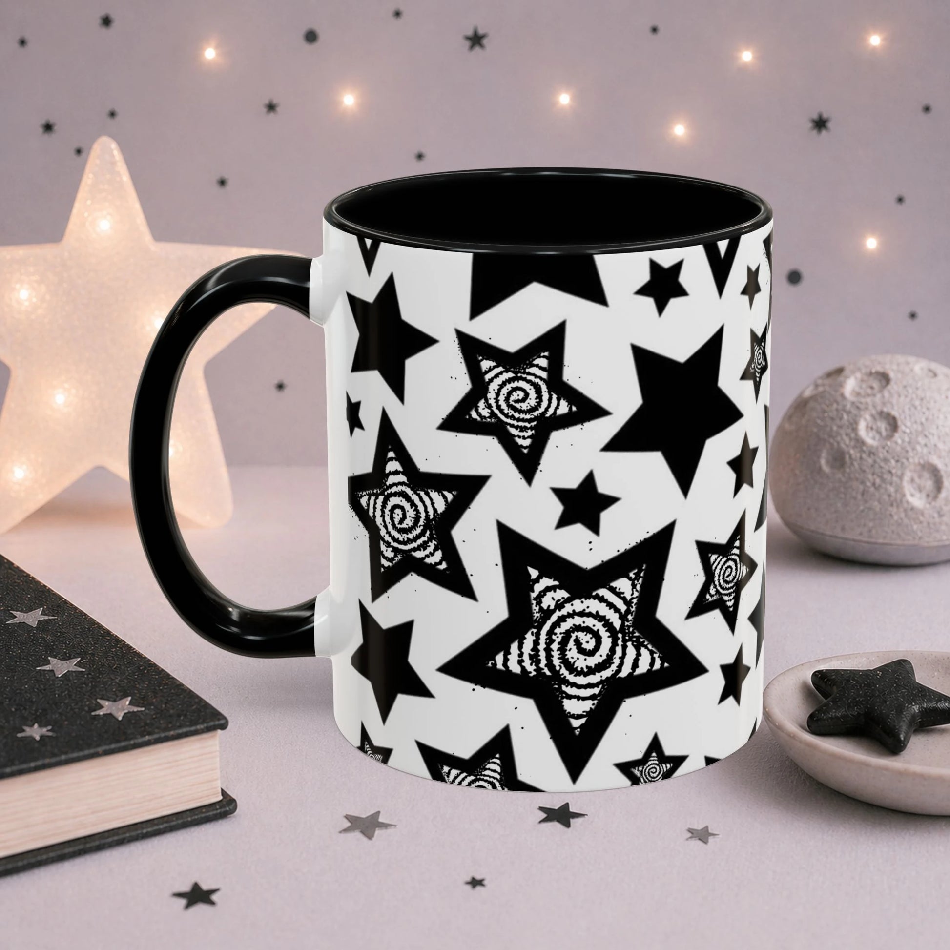 Monochrome star mug with repeating black celestial stars and spiral artwork, black accent handle and interior, photographed in a cozy cosmic scene.