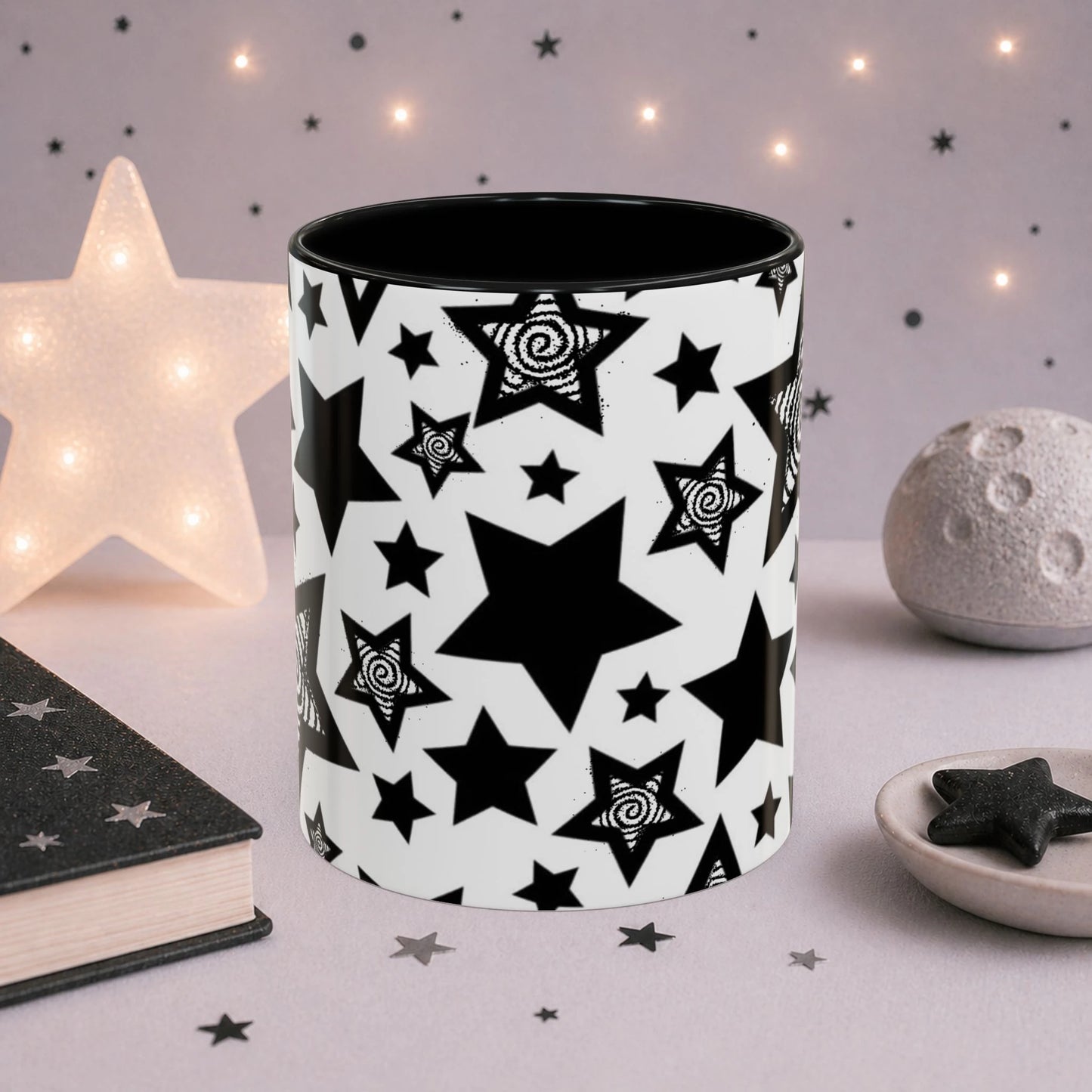 Black and white star pattern mug with hypnotic spiral stars, black handle and interior, displayed in a dreamy celestial setting with moon decor and soft star lights.