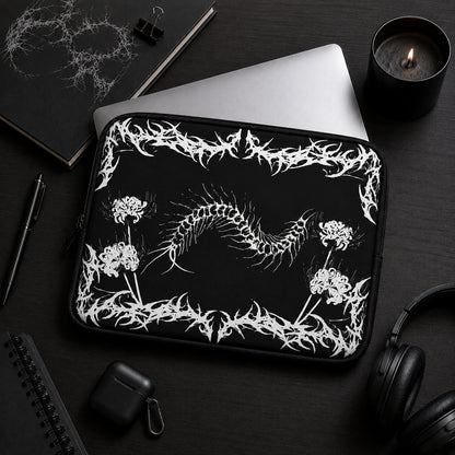 Gothic centipede laptop sleeve featuring spider lily flowers and black metal inspired artwork, displayed in a dark aesthetic workspace with laptop, headphones and black accessories.