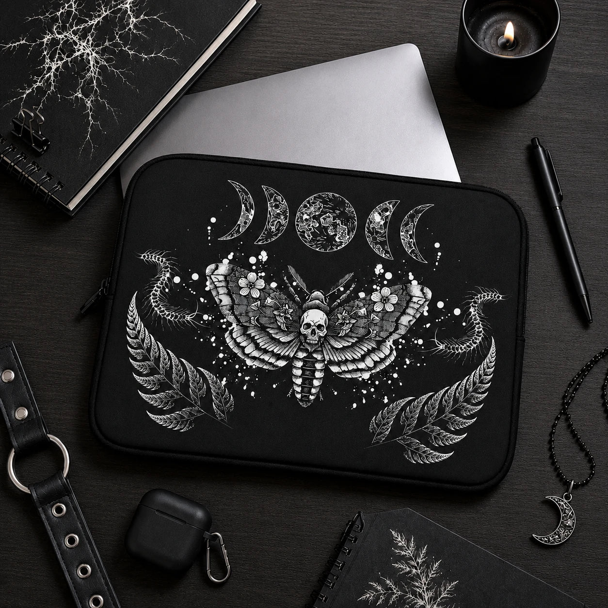 Gothic death moth laptop sleeve featuring skull moth artwork, moon phases and centipede illustrations, displayed in a dark alternative workspace with black accessories.