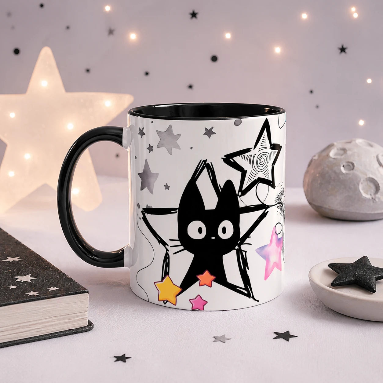 Black cat aesthetic mug with colorful stars, black handle and interior, displayed in a dreamy celestial setup with star lights, moon decor and soft pastel background.