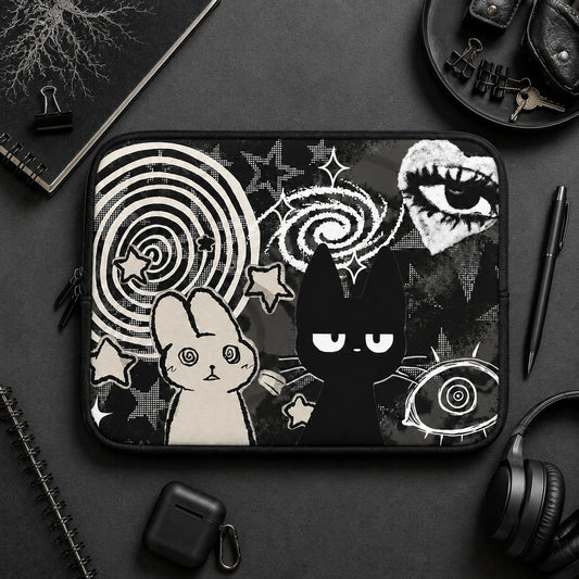 Gothic aesthetic laptop sleeve with black cat and hypnotic bunny illustration displayed on a dark desk setup with headphones, notebook and alternative lifestyle accessories. 