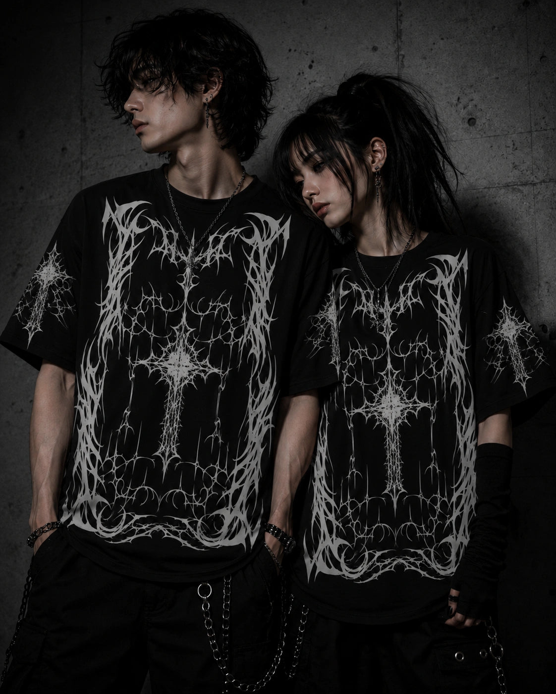 Alternative fashion couple wearing matching oversized black gothic cross graphic t-shirts with white black-metal inspired artwork.