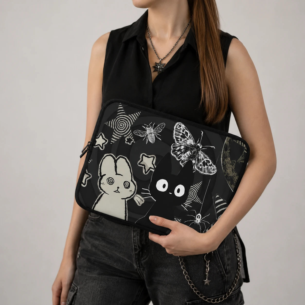 Gothic kawaii laptop sleeve with black cat, bunny, butterfly, moon and star illustrations displayed on a dark aesthetic desk with alternative accessories and laptop. 