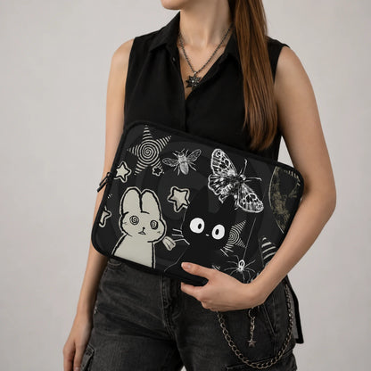 Gothic kawaii laptop sleeve with black cat, bunny, butterfly, moon and star illustrations displayed on a dark aesthetic desk with alternative accessories and laptop. 