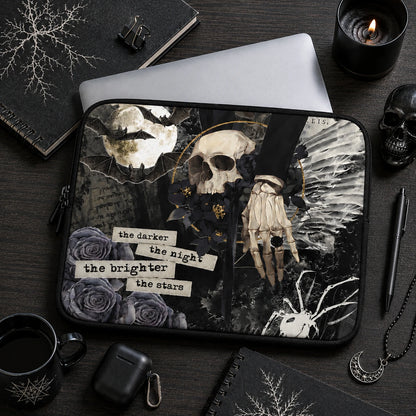 Dark gothic laptop sleeve with skull, bats, black roses and skeletal hand illustration displayed in a moody black desk setup with candles, notebooks, coffee mug and alternative lifestyle accessories.