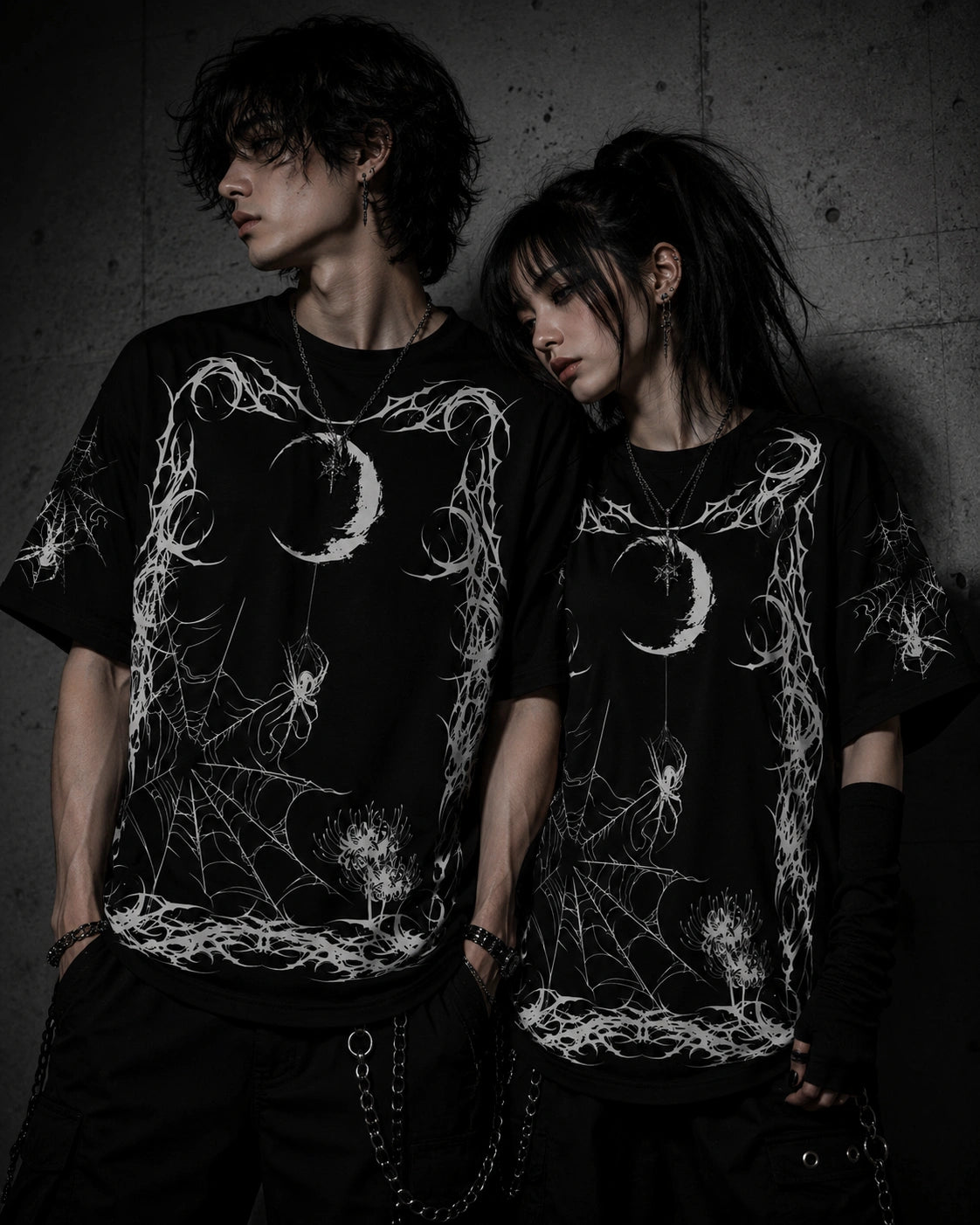 Alternative fashion couple wearing matching oversized gothic spider web graphic t-shirts with moon and spider artwork.