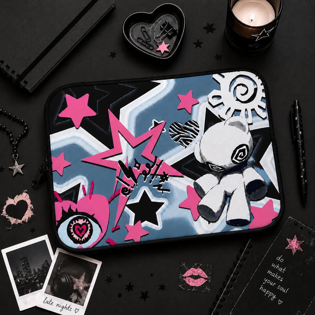 Pastel goth laptop sleeve flat lay surrounded by black aesthetic stationery, candle and alternative decor, featuring pink stars, grunge artwork and cute voodoo doll design.