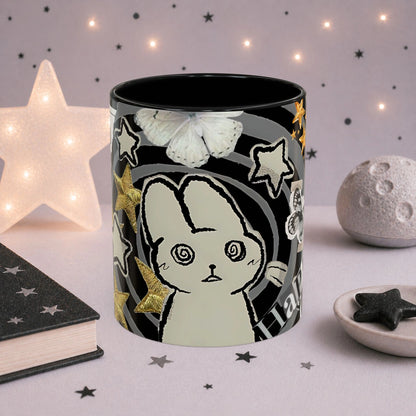 Close-up of weirdcore cat mug with spiral eyes, gold stars, butterfly details and black and white collage aesthetic design.