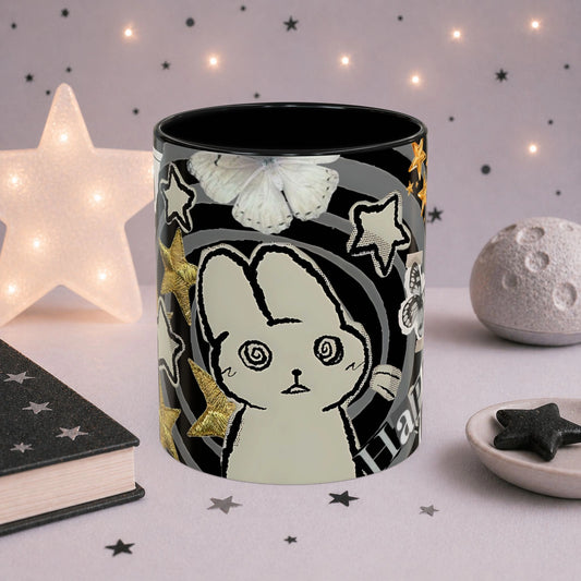 Close-up of weirdcore cat mug with spiral eyes, gold stars, butterfly details and black and white collage aesthetic design.